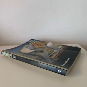 May include: A black hardback book titled "Dali The Impossible Dream of Surrealism" by Thames & Hudson. The book cover features a painting of a surreal landscape with a large white bird.