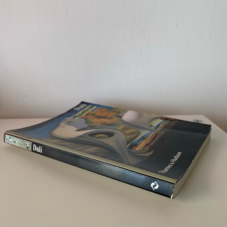 May include: A black hardback book titled "Dali The Impossible Dream of Surrealism" by Thames & Hudson. The book cover features a painting of a surreal landscape with a large white bird.