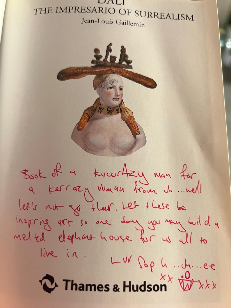 May include: A book titled "The Impresario of Surrealism" by Jean-Louis Gaillemin with a handwritten note on the cover that reads "Book of a kuwrAzy man for a kerrazy vuman from un....wel let's not go ther. Let these be inspiring art so one day you may build a meled elephant house for us all to live in. Luv Soph..ch...ee xxx"