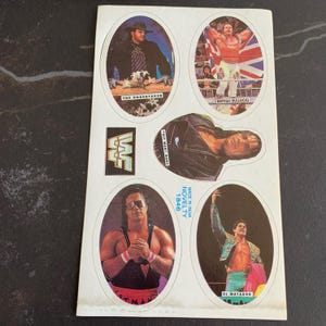 May include: A sheet of vintage WWF wrestling stickers. The stickers feature images of wrestlers like The Undertaker, British Bulldog, and El Matador. The WWF logo is also visible. The sheet is labeled "Made in India Novelty 1846."