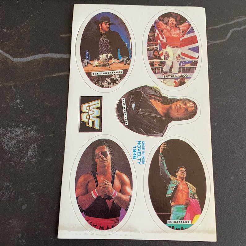 May include: A sheet of vintage WWF wrestling stickers. The stickers feature images of wrestlers like The Undertaker, British Bulldog, and El Matador. The WWF logo is also visible. The sheet is labeled "Made in India Novelty 1846."