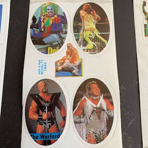 May include: A sheet of vintage wrestling stickers featuring colorful illustrations of wrestlers in action. The stickers include images of a clown, a wrestler in a yellow outfit, and others. The text "The Warlord" is visible on one sticker.