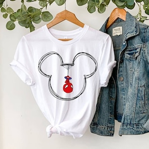 May include: White t-shirt featuring a black and white outline of Mickey Mouse's head. Spider-Man is hanging upside down from a web inside the outline.