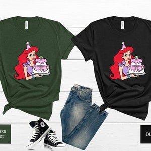 Pode incluir: Duas camisetas com uma imagem de desenho animado de Ariel da Pequena Sereia segurando um bolo de anivers&aacute;rio rosa e branco. As camisetas s&atilde;o em verde floresta heather e preto.