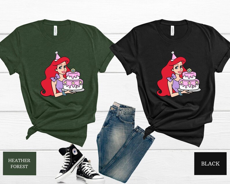 Pode incluir: Duas camisetas com uma imagem de desenho animado de Ariel da Pequena Sereia segurando um bolo de anivers&aacute;rio rosa e branco. As camisetas s&atilde;o em verde floresta heather e preto.
