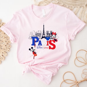 Pu&ograve; includere: Maglietta rosa con una grafica di Topolino e Minnie Mouse davanti alla Torre Eiffel e il testo "Paris Disneyland".