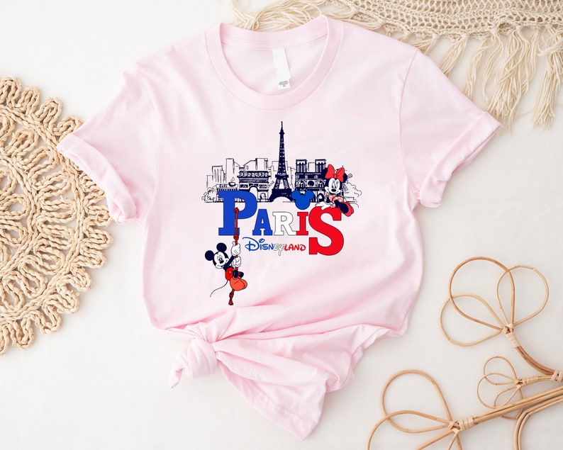 Pu&ograve; includere: Maglietta rosa con una grafica di Topolino e Minnie Mouse davanti alla Torre Eiffel e il testo "Paris Disneyland".