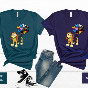 May include: Two t-shirts featuring a cartoon dog holding balloons with Disney character faces. The t-shirts are in deep teal and navy blue.