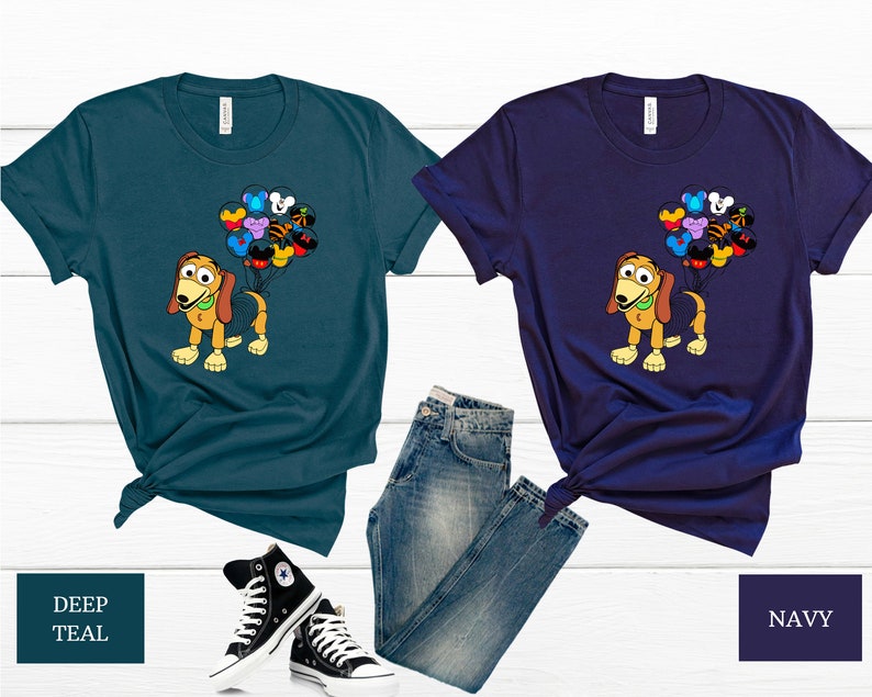 May include: Two t-shirts featuring a cartoon dog holding balloons with Disney character faces. The t-shirts are in deep teal and navy blue.