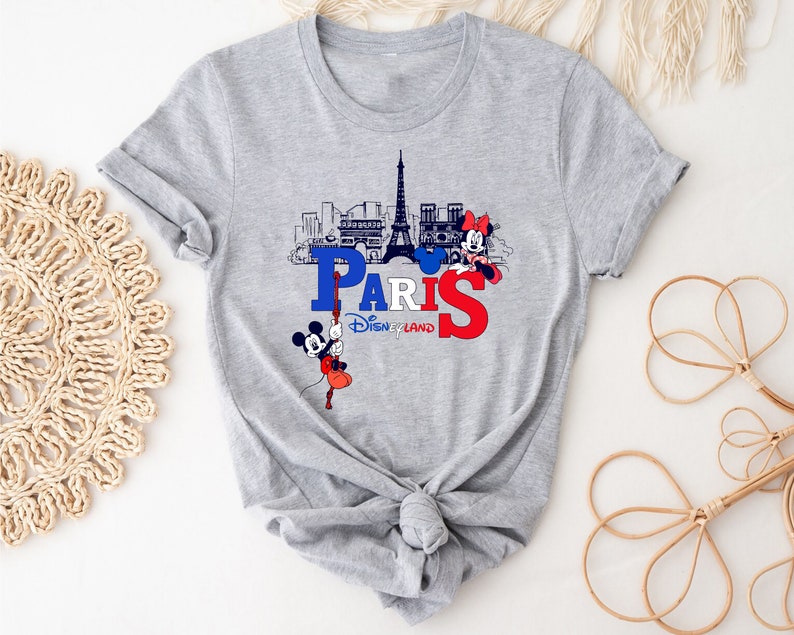 Pu&ograve; includere: Maglietta grigia con una grafica di Topolino e Minnie Mouse davanti alla Torre Eiffel. Il testo "Paris Disneyland" &egrave; stampato sulla maglietta.