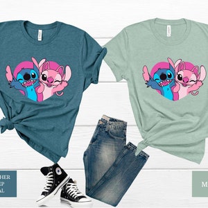 以下が含まれることがあります： リロ＆スティッチのスティッチとエンジェルがプリントされたグラフィックTシャツ2枚。左側のTシャツはヘザーディープティールカラー、右側のTシャツはミントグリーンカラーです。