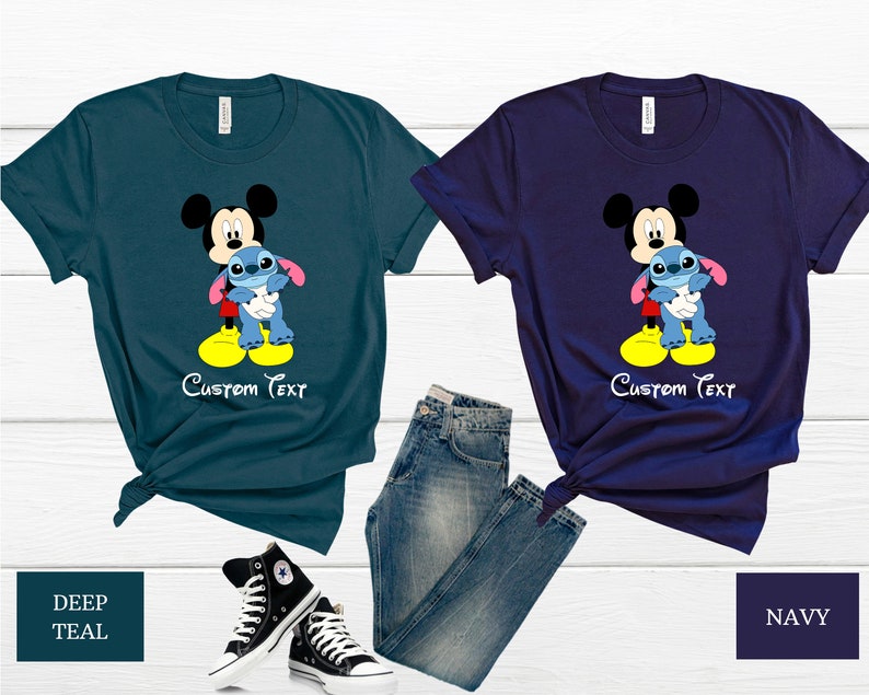 May include: Two t-shirts featuring Mickey Mouse holding Stitch. The shirt on the left is teal and the shirt on the right is navy. Both shirts have the text "Custom Text" printed on them.