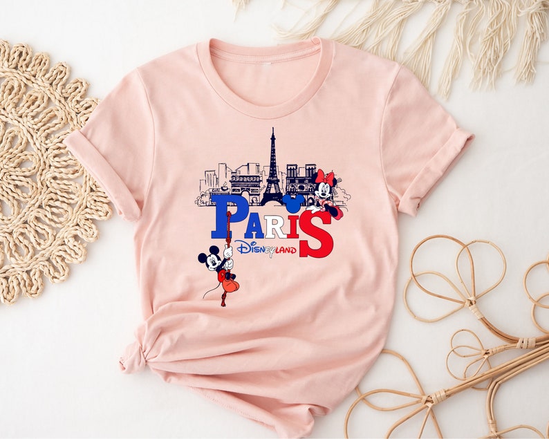 Pu&ograve; includere: Maglietta rosa con una grafica di Topolino e Minnie Mouse di fronte alla Torre Eiffel e il testo "Paris Disneyland".