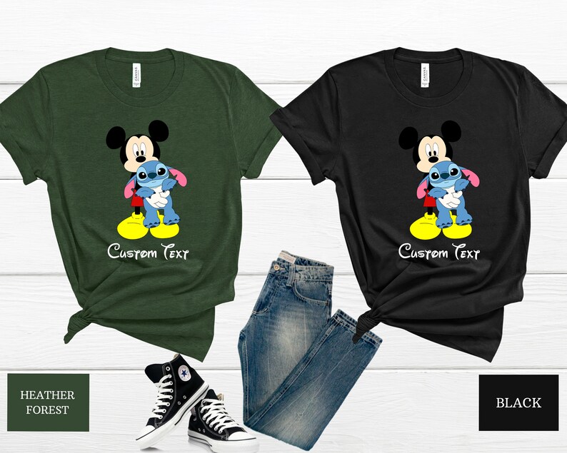 May include: Two t-shirts featuring Mickey Mouse and Stitch. The shirt on the left is a heather forest green colour and the shirt on the right is black. Both shirts have the text "Custom Text" printed on them.