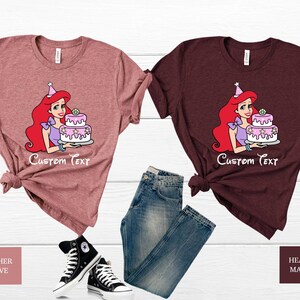 Pode incluir: Duas camisetas com uma imagem de desenho animado de Ariel da Pequena Sereia segurando um bolo de anivers&aacute;rio rosa e branco. O texto "Custom Text" &eacute; impresso abaixo da imagem. A camiseta &agrave; esquerda &eacute; de cor malva mesclada e a camiseta &agrave; direita &eacute; de cor marrom mesclada.