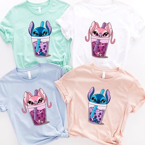 May include: Four t-shirts in pastel colors: mint green, white, light blue, and peach. Each shirt features a cartoon character in a boba drink cup with purple boba pearls and a straw. The characters are blue and pink.
