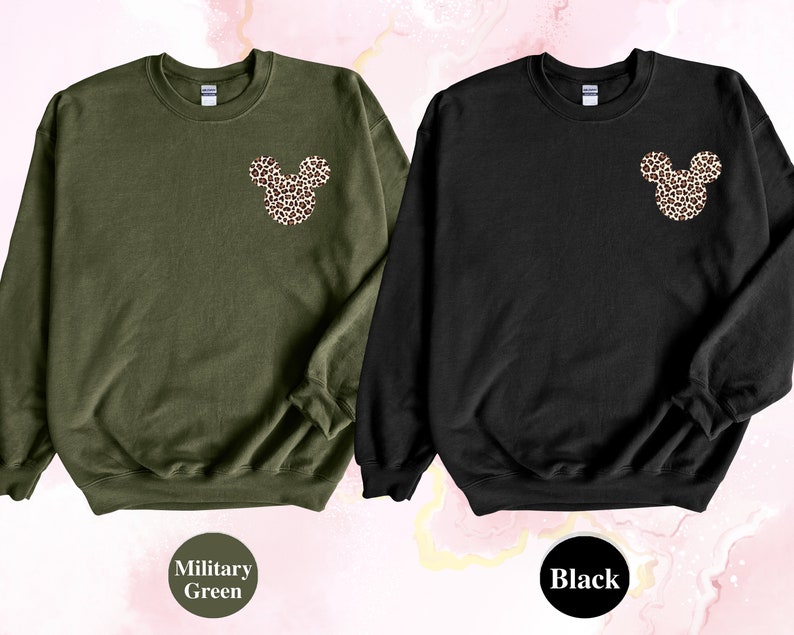 May include: Two crewneck sweatshirts, one military green and one black. Each features a leopard print Mickey Mouse head design on the upper left chest. The military green sweatshirt has the words "Military Green" in a circle below it, and the black sweatshirt has the word "Black" in a circle below it.