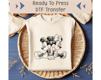 May include: A white t-shirt with a black and white illustration of Mickey Mouse and Minnie Mouse. The text "Ready To Press DTF Transfer" is at the top of the shirt.