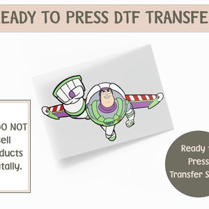 May include: A ready-to-press DTF transfer sheet featuring a cartoon image of Buzz Lightyear in flight. The character is primarily white, green, and purple, with red and white accents. Text on the image includes "Ready to Press Transfer Sheet."
