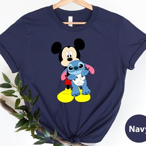 May include: Navy blue t-shirt featuring Mickey Mouse holding Stitch, a blue alien character. The shirt has a casual, relaxed fit.