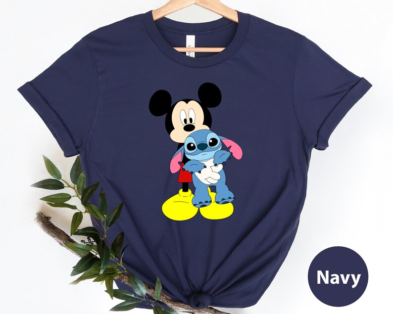 May include: Navy blue t-shirt featuring Mickey Mouse holding Stitch, a blue alien character. The shirt has a casual, relaxed fit.