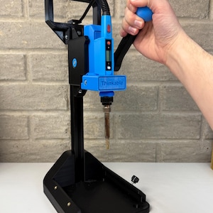 May include: A black and blue soldering station with the word "Thinkable" printed on the front. The station has a blue handle and a digital display. The base is black and rectangular, and the soldering iron is visible.