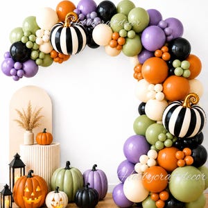 May include: A balloon arch featuring orange, purple, black, olive green, and cream balloons with two black and white striped pumpkin balloons. Below are several decorative pumpkins in orange, green, purple, and black, including two lit jack-o'-lanterns.