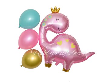May include: Pink dinosaur shaped foil balloon with a gold crown, pink heart designs, and a smiling face.  Three additional balloons are included: one light blue, one pink, and one gold.