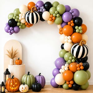 May include: A balloon arch featuring orange, purple, olive green, black, and cream balloons with two black and white striped pumpkin balloons. Below, several decorative pumpkins in orange, green, purple, and black sit near two black lanterns.
