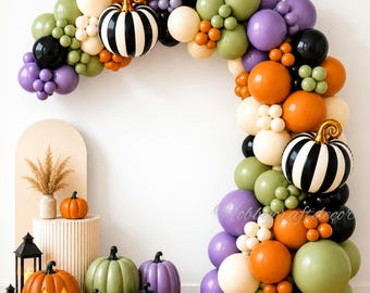 May include: A balloon arch featuring orange, purple, olive green, black, and cream balloons with two black and white striped pumpkin balloons. Below, several decorative pumpkins in orange, green, purple, and black sit near two black lanterns.
