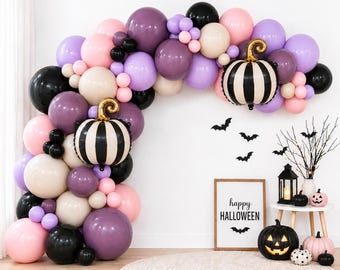 Op de afbeelding: Een Halloween-ballonnenboog met een mix van zwarte, paarse, lichtroze en beige ballonnen. Twee gestreepte pompoenvormige folieballonnen zijn geïntegreerd. Een bord toont de tekst happy HALLOWEEN met vleermuisstickers, pompoenen en een lantaarn.