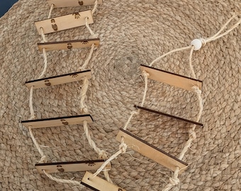 May include: A hanging wooden ladder toy featuring two parallel vertical jute ropes connected by several horizontal light-colored wooden slats. Each slat is engraved with small, dark brown icons of footprints and handprints, with a single white bead.