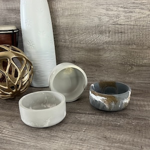 May include: Three concrete bowls, one with a white and gray marbled finish, one with a gray and gold marbled finish, and one with a plain gray finish.