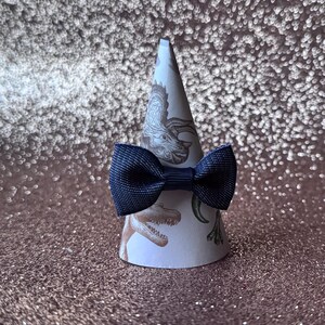 May include: A navy blue bow tie on a white cone with a dinosaur print.