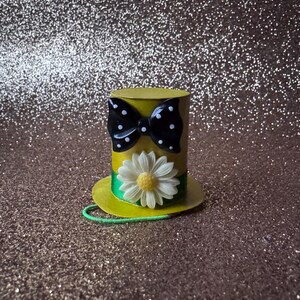 May include: A yellow top hat with a black and white polka dot bow and a white daisy with a yellow center. The hat has a green ribbon around the base.
