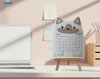 May include: A cat-shaped 2026 October calendar on a small wooden easel. The calendar has a white background with black numbers and dates. The cat design features a gray face and ears. The text "2026 Cat printable calendar" is at the bottom.