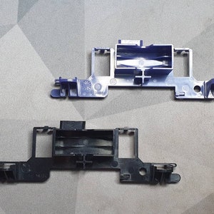 May include: Two plastic electronic components. One is a dark navy blue color, and the other is black. Both components have a rectangular shape with various protrusions and openings. The navy blue component has the text "ABS" printed on it.