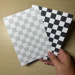 May include: Two rectangular cards with rounded corners, one featuring a light gray and white checkered pattern and the other displaying a high-contrast black and white checkered pattern, both arranged in a grid layout on a flat surface.