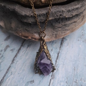 May include: A purple amethyst crystal pendant necklace with an ornate bronze filigree setting. The necklace is on a chain with a bronze finish.