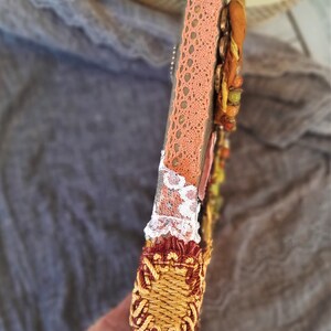 May include: A wooden frame with a decorative design featuring a peach-colored lace trim, white lace, and a gold and red woven trim. The frame is decorated with beads and other embellishments.