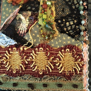 May include: A handmade journal cover with a variety of textures and embellishments, including lace, beads, and fabric. The cover is decorated with a star, a hand, and a beaded necklace.