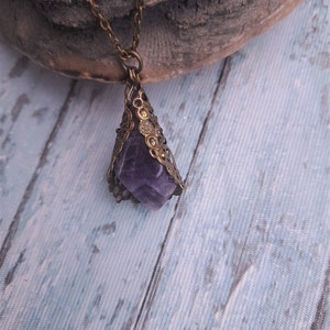 May include: A purple amethyst crystal pendant with a gold filigree frame, hanging from a gold chain.