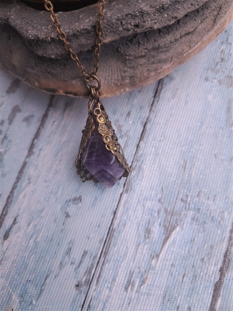 May include: A purple amethyst crystal pendant with a gold filigree frame, hanging from a gold chain.
