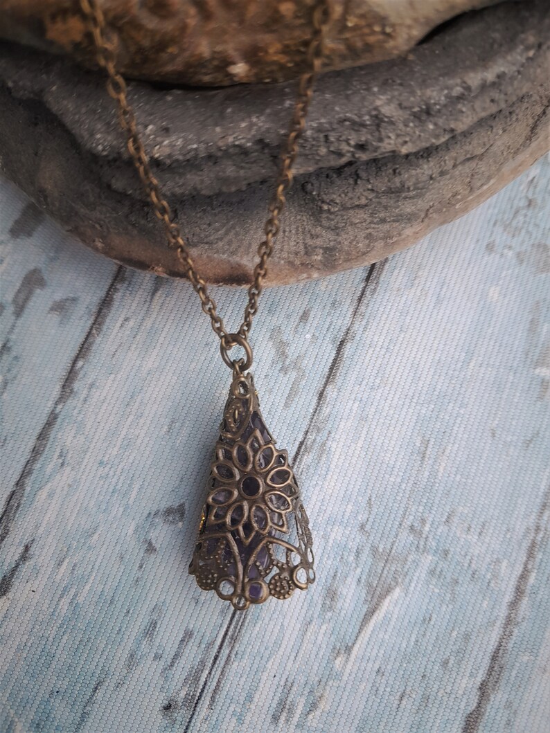 May include: A delicate gold chain necklace with a pendant featuring a purple amethyst stone encased in an intricate filigree design.