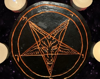 May include: A black wooden circle with an orange pentagram featuring a goat's head in the center. The circle is surrounded by four white candles.
