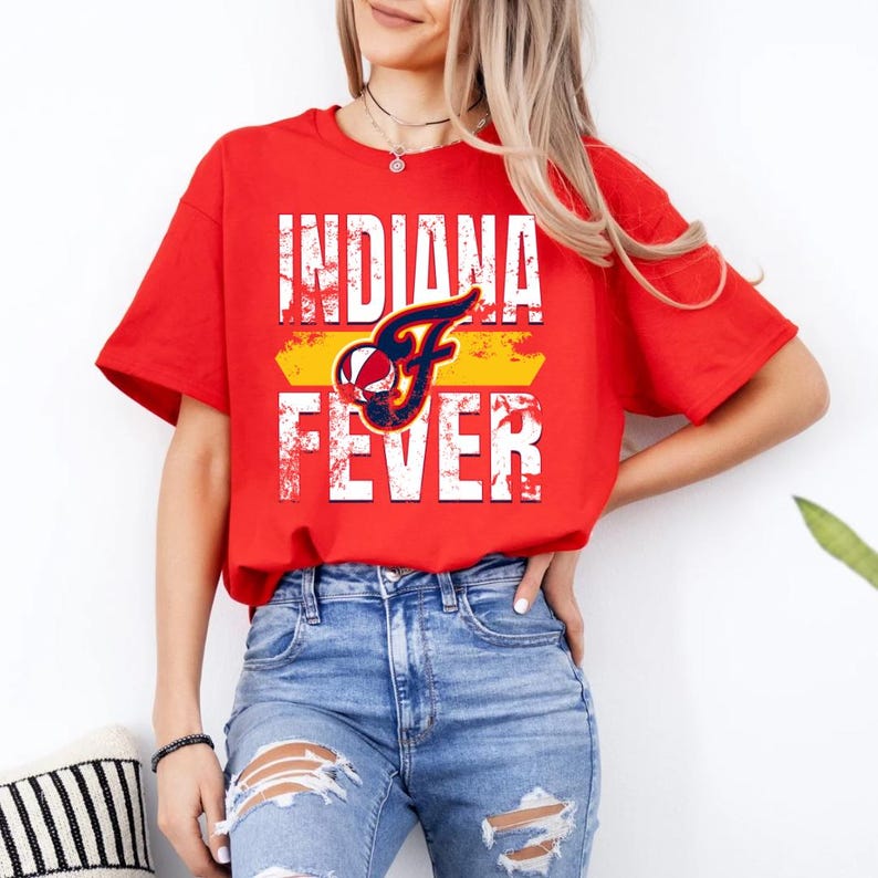 Puede incluir: Una camiseta roja de manga corta con el texto blanco desgastado INDIANA FEVER y un gr&aacute;fico central de un bal&oacute;n de baloncesto y una letra F estilizada en azul marino, naranja y blanco, combinada con unos vaqueros azul claro desgastados.