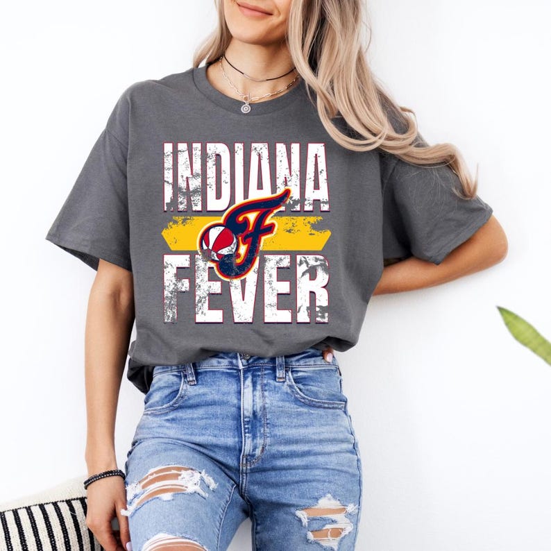 Puede incluir: Una camiseta gris carb&oacute;n de manga corta con un estampado gr&aacute;fico desgastado que dice INDIANA FEVER en letras blancas. Una letra F estilizada en azul marino y rojo incorpora un dise&ntilde;o de baloncesto sobre una barra amarilla.