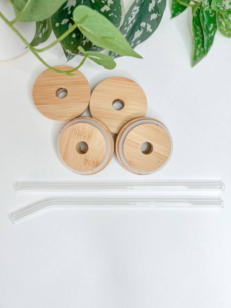 May include: A set of four bamboo lids with a hole and two clear glass straws. The lids have a natural wood grain finish and a silicone seal. The straws are straight and bent. The items are arranged on a white surface.