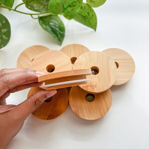 May include: A collection of round bamboo lids with a central hole, some stacked, others scattered. One lid is held up, revealing a white silicone seal. The lids are light brown, with a natural wood grain. The background is white.