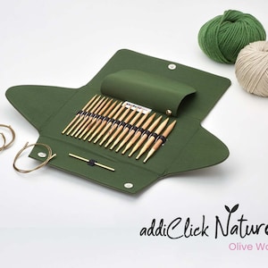 Könnte beinhalten: Ein Set addiClick Nature Interchangeable Stricknadeln aus Olivenholz, mit einer grünen Tragetasche und zwei Wollknäuel. Die Nadeln sind in der Tasche angeordnet, mit den Spitzen nach oben. Die Tasche hat einen Reißverschluss und ein kleines Etikett mit der Aufschrift "addiClick Nature Olive Wood".